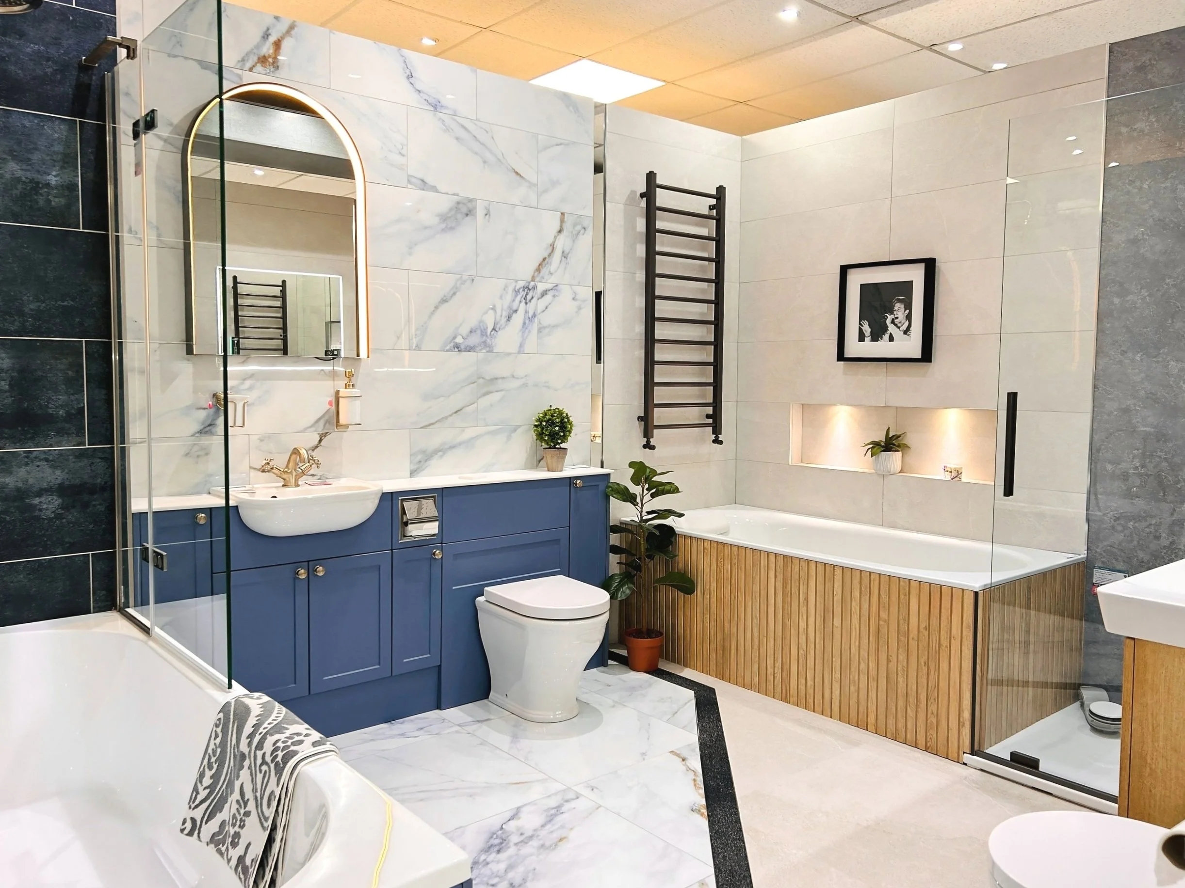 Luxury bathroom showroom featuring a blue vanity unit, marble-effect wall tiles, walk-in shower, modern bath, illuminated mirror, and contemporary bathroom design in Bournemouth and Salisbury.